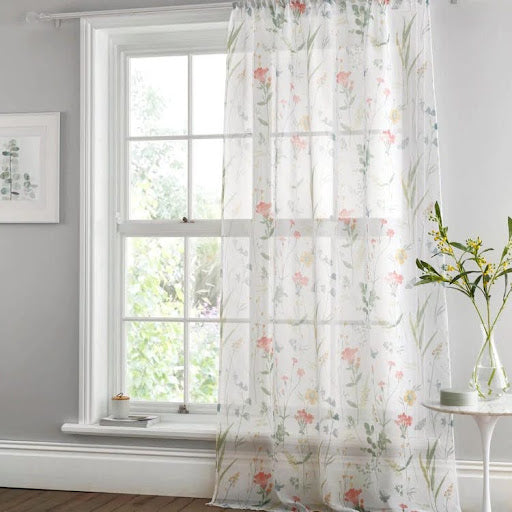A sash and case window looking out onto a spring garden, with a meadow print single voile panel in pastel shades of pink, yellow and green.